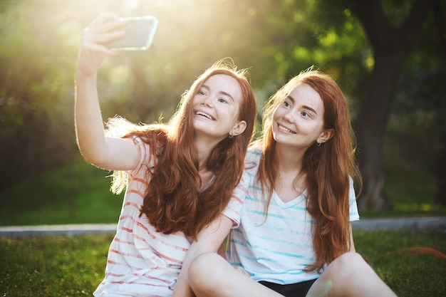 Free photo ginger twin girls taking a selfie on a smart phone, smiling rejoicing. modern technology connects people more than ever. having a distant friend is so much fun.