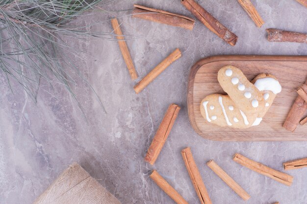 Gingerbread cookies with cinnamon sticks on long wooden board.