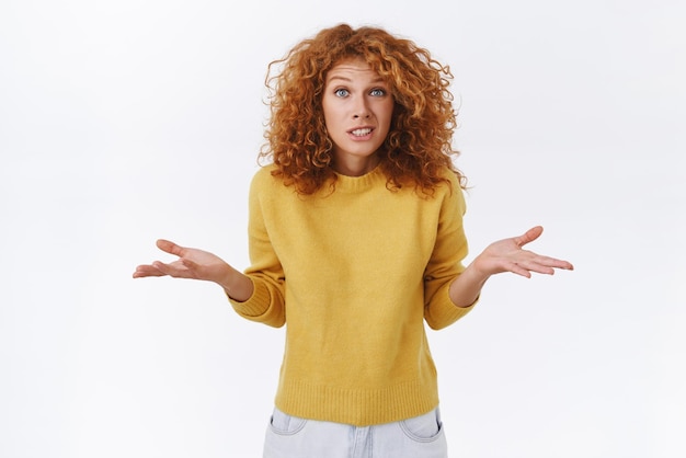 Girl apologizing shrugging as dont know cant help Cute silly and awkward redhead woman in yellow sweater spread arms sideways smiling clumsy and embarrassed admit her fault white background