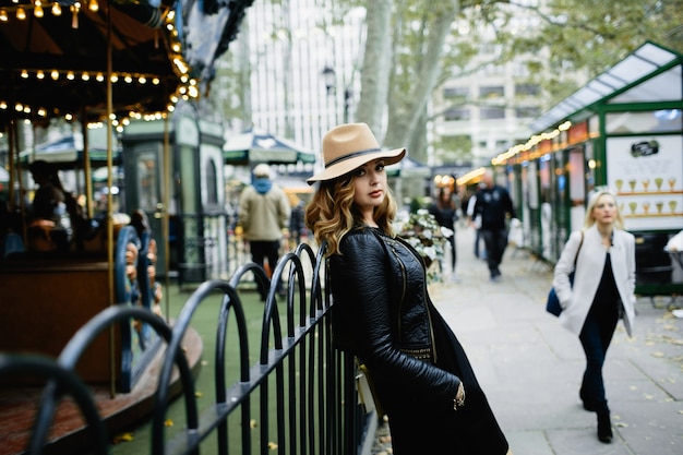 Girl in beige hat leans to steel fence on the street