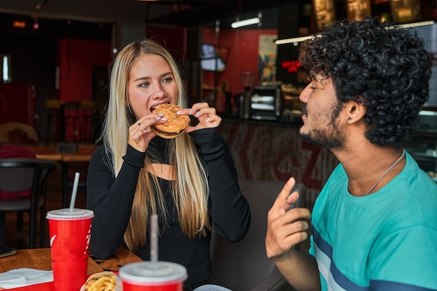 Girl bites burger in cafe with her boyfriend.