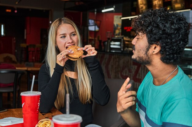 Girl bites burger in cafe with her boyfriend.