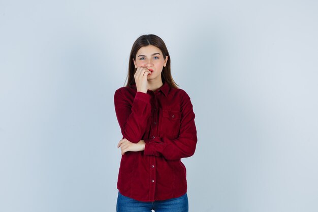 girl biting nails in burgundy blouse and looking thoughtful