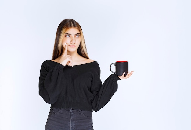 Free Photo girl in black shirt holding a black coffee mug and thinking. high quality photo