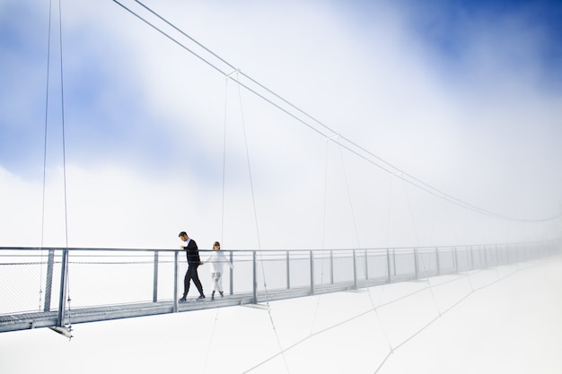 Girl and boy walking on bridge in clouds