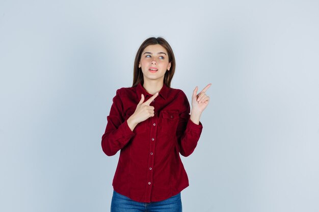 Girl in burgundy blouse pointing at upper right corner and looking confident