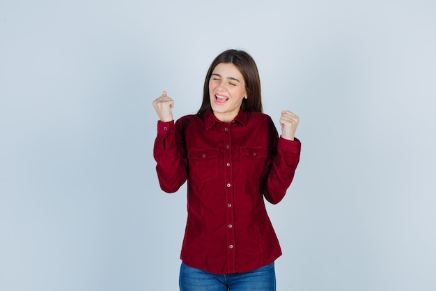 girl in burgundy shirt showing winner gesture and looking blissful