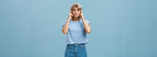 Free photo girl cannot concentrate hearing loud noise comming from upstairs frowning feeling intense and dissatisfied closing ears with index fingers looking up while complaining on awful sound over blue wall