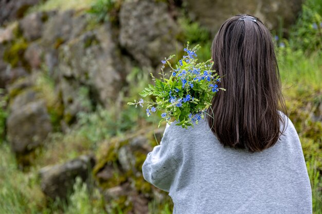 The girl carries a bouquet of flowers collected in the spring forest, view from the back