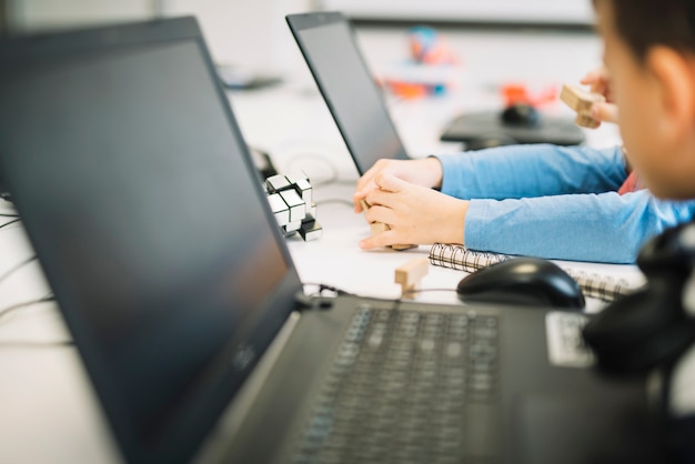 A girl child playing with wooden cube puzzle with laptop on white desk