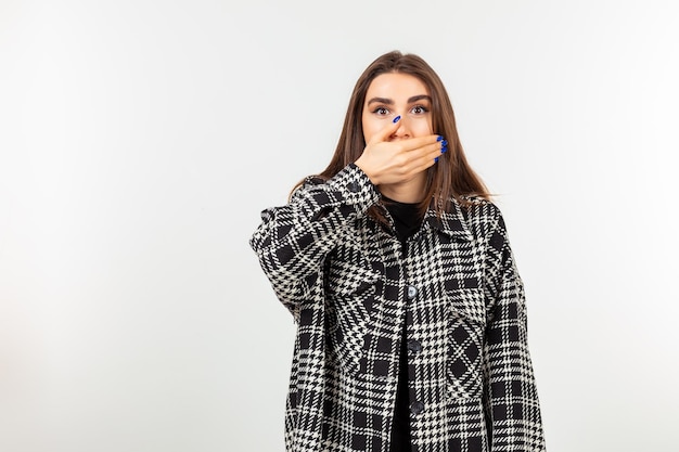 A girl closed her mouth with her hand and standing on white background