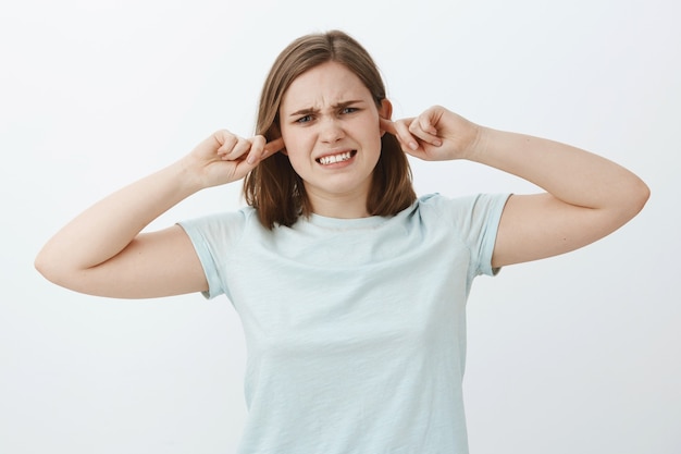 Girl closes ears feeling displeased when people fight near her. Intense dissatisfied young female clenching teeth from discomfort feeling bothered from loud sound covering hearing with earplugs