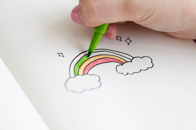 Girl coloring a rainbow doodle in a notebook