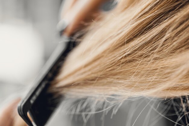 Girl combing blonde hair with a brush. Closeup