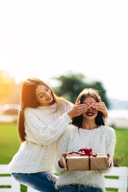 Girl covering her eyes with another girl with a gift in her hands