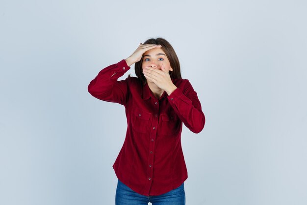 girl covering mouth, keeping hand over head in casual shirt and looking surprised.