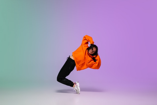 Free photo girl dancing hip-hop in stylish clothes on gradient background at dance hall in neon light.