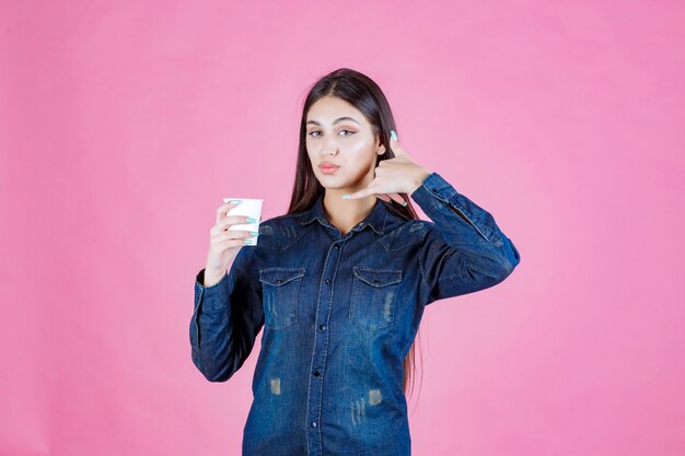 Girl in denim shirt holding a coffee cup and making call sign