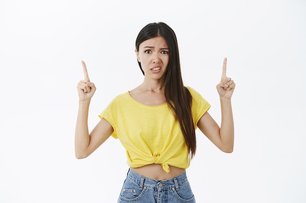 Girl does not like what see. Displeased awkward and unimpressed good-looking female in yellow t-shirt raising hands pointing up