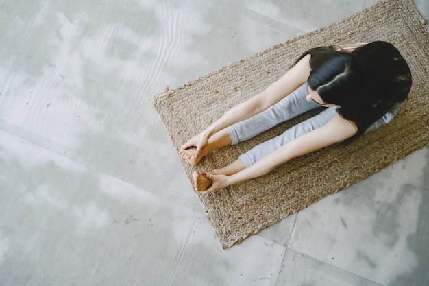 Girl doing yoga exercises at home near sofa and window in sportswear