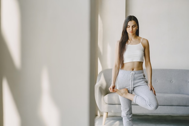 Free photo girl doing yoga exercises at home near sofa and window in sportswear