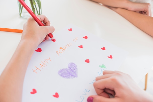 Free photo girl drawing red hearts on paper with happy mothers day inscription