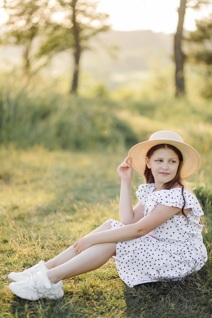 A girl in a dress and a hat stands in the field