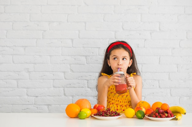 Girl drinking strawberry smoothies with colorful fruits on the desk