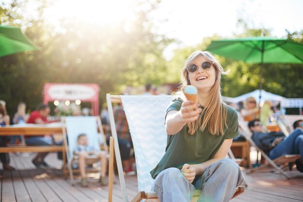 Free Photo girl eating ice cream laughing portrait of young woman sitting in a park on a sunny day eating icecream looking on camera wearing glasses enjoying summer proposing to camera summer lifestyle concept