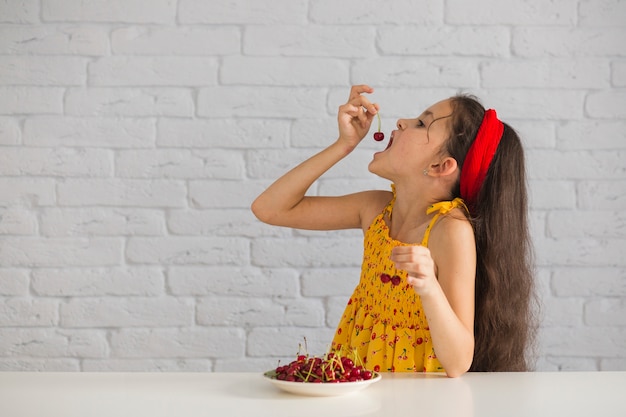 Girl eating red fresh cheery in front of brick wall