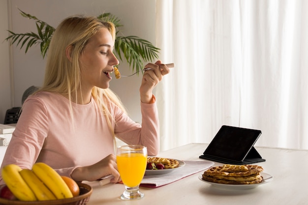 Free photo girl eating waffles watching tablet