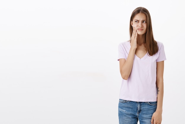 Girl feeling discomfort in mouth having decay standing bothered and displeased after sipping cold drink looking left touching cheek and frowning from toothache posing