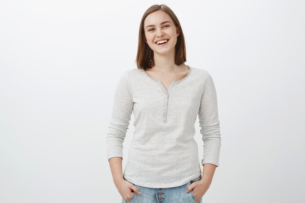 Girl feeling happy being teenager and living carefree life. Portrait of sociable friendly-looking charming female brunette holding hands in pockets casually and smiling joyfully