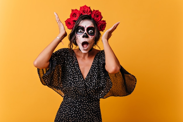 Girl from Latin America with skull makeup reacts emotionally and poses for portrait in orange wall