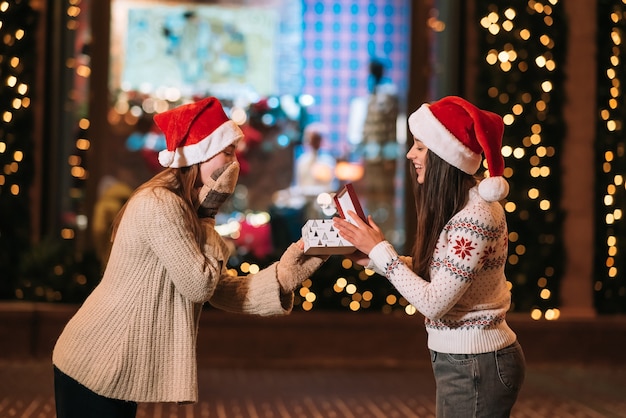 The girl gives a gift to her female friend on the street. Portrait of happy cute young friends