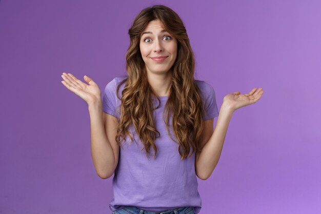 Girl not giving any care. Carefree unbothered cute caucasian curly-haired woman shrugging hands spread sideways smirking uninterseted nothing to say shake head questioned clueless purple background