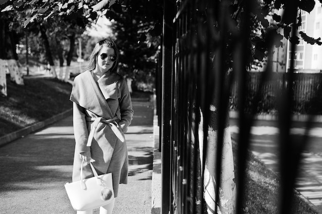 Free Photo girl in gray coat with sunglasses and handbag walking at street against iron fence