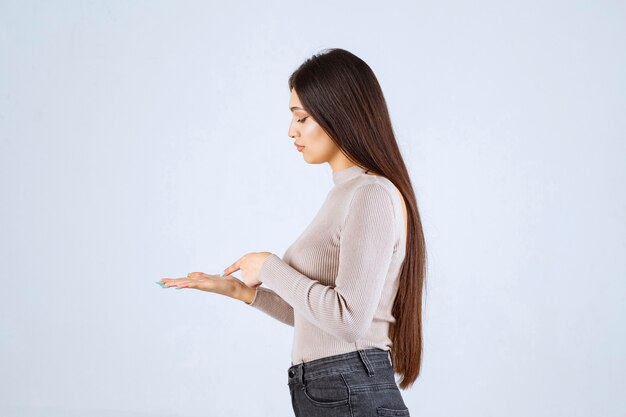 Girl in grey sweater looking to something at her hand. 