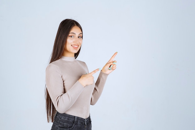 Girl in grey sweater pointing something above.