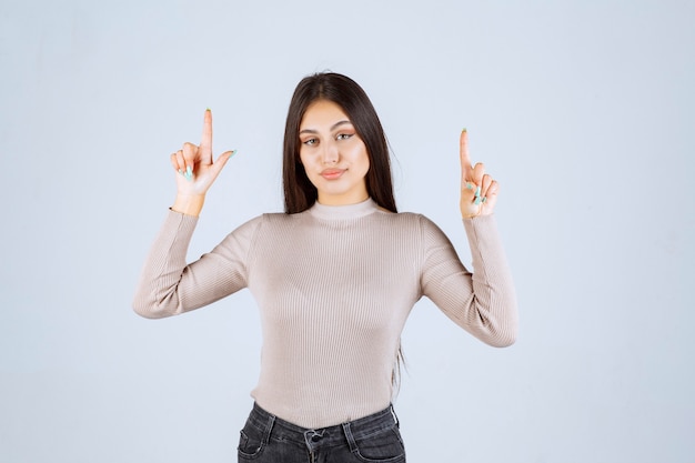 Girl in grey sweater pointing something above. 