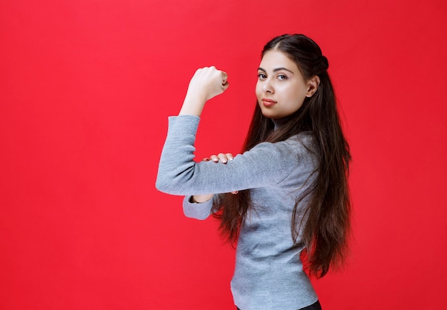 Girl in grey sweater showing her arm muscles.