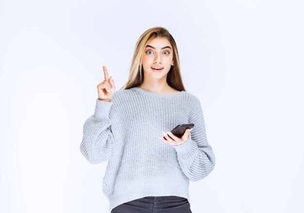 Girl in grey sweatshirt holding a black smartphone and has a good idea.