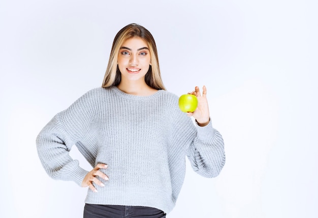 Girl in grey sweatshirt holding green apple in the hand.