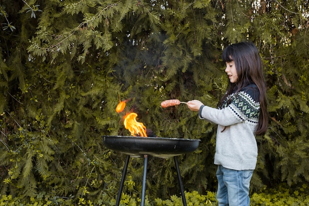 Free photo girl grilling barbecue sausages in front of tree