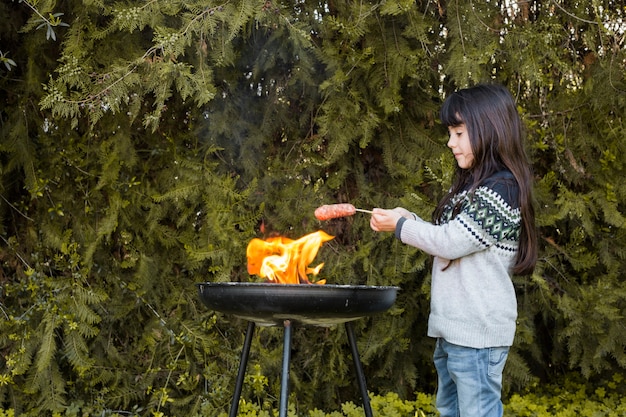 Girl grilling sausages over the flame on outdoor barbecue