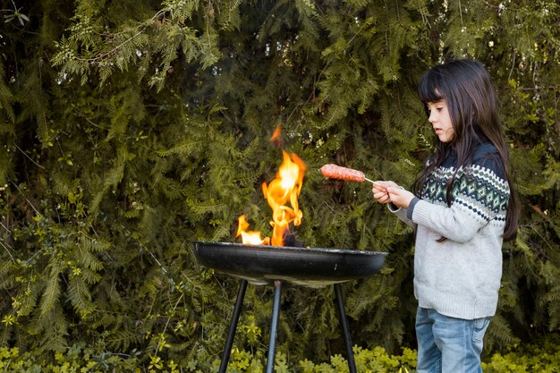 Girl grilling sausages on outdoor barbecue