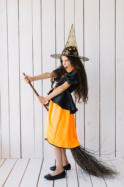 Free photo girl in halloween costume imitating broom flight in studio