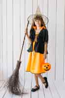 Free photo girl in halloween costume with basket and broom posing in studio