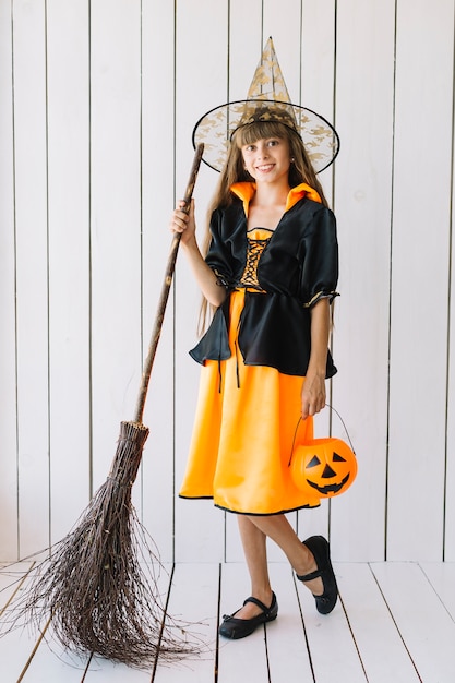 Girl in Halloween costume with basket and broom posing in studio