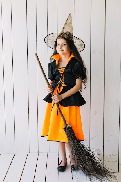 Girl in Halloween costume with broom posing in studio